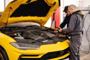 two-mechanics-stand-with-tbalet-against-open-hood-of-yellow-sport-car-suv-.jpg